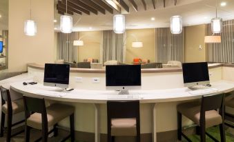 a modern office space with multiple computer monitors on a white desk , surrounded by large windows and comfortable seating at Even Hotel Rockville - Washington DC Area