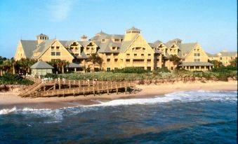 a large , yellow house situated on the beach with a boardwalk extending into the ocean at Disney's Vero Beach Resort