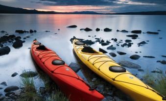 two red and yellow kayaks are parked on a rocky shore near the water , with a cloudy sky in the background at Peninsula Motel