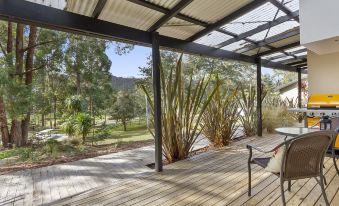 a wooden deck with a metal roof overlooks a lush green field and trees in the distance at Oyster Cove Chalet