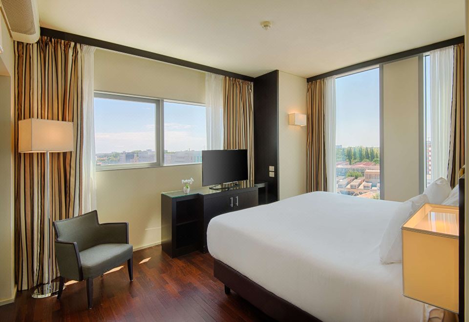 a hotel room with a large bed , a television , and a window overlooking the city at NH Padova