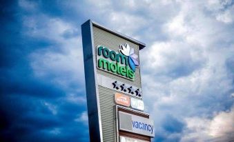 a large , illuminated sign for the rooms motel with a vacancy sign and a blue sky background at Room Motels Gympie