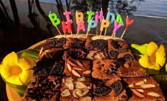 a birthday cake with a variety of brownies , placed on a wooden table near the water at Phayamas Private Beach Resort and Island Brew - Adults Only