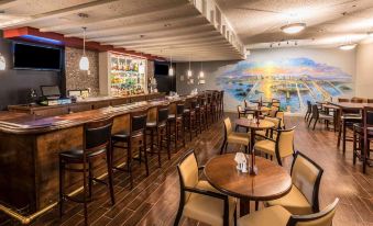 a well - lit restaurant with wooden tables and chairs , a bar , and a large mural on the wall at Penn Harris Hotel Harrisburg, Trademark by Wyndham