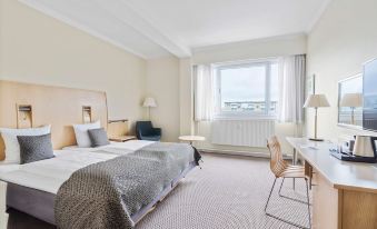 a hotel room with a large bed , a desk , a chair , and a window overlooking the city at Best Western Plus Airport Hotel Copenhagen