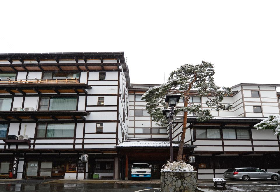 a building with a tree in front of it and cars parked on the side at Osakaya Ryokan