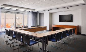 a conference room with a long table and chairs , a large screen on the wall , and windows at Aloft Leawood-Overland Park