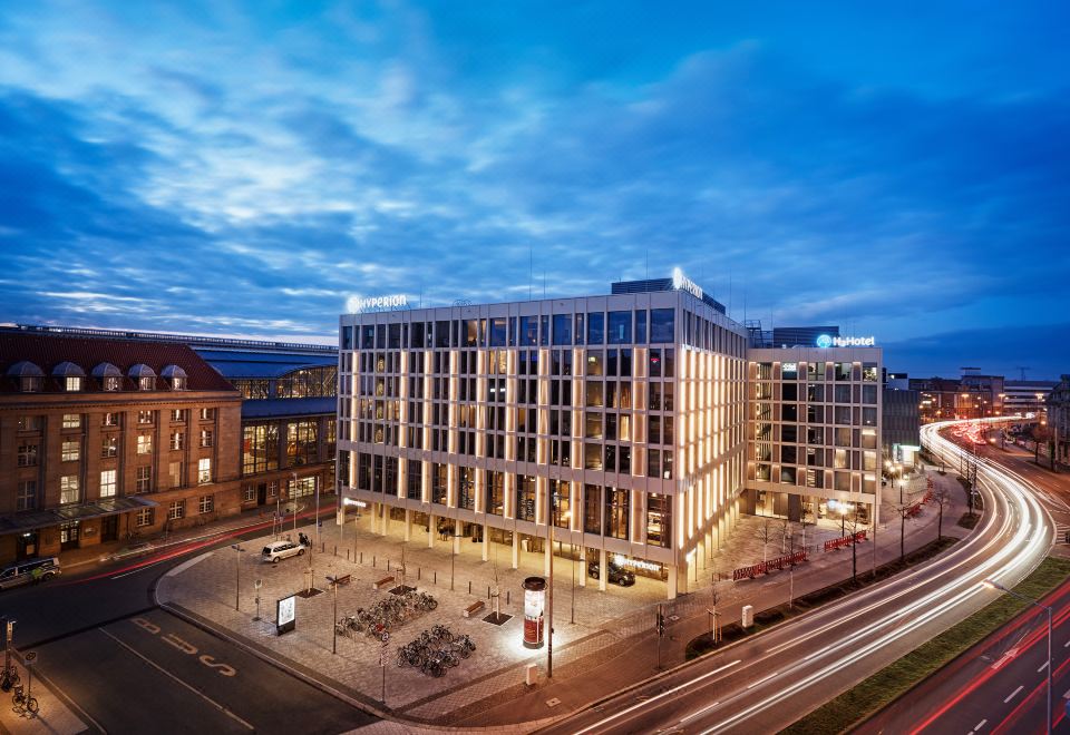 a modern building with multiple floors and large windows is illuminated by street lights at night at HYPERION Hotel Leipzig