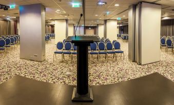 a conference room with blue chairs and a podium in the center , surrounded by white walls at Galaxy Hotel
