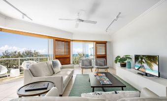 a modern living room with a white couch , coffee table , and large windows overlooking the ocean at Rolling Surf Resort Sunshine Coast