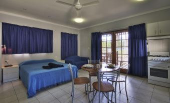 a hotel room with a blue bed , wooden dining table , and chairs , as well as a balcony overlooking the ocean at Cairns Sunland Leisure Park