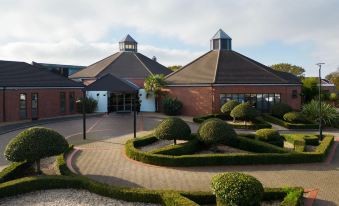 a large , modern building with a curved design and a circular driveway surrounded by greenery at Delta Hotels Waltham Abbey