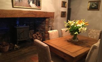 a dining room with a wooden table and chairs , a fireplace , and a painting on the wall at Primrose Cottage
