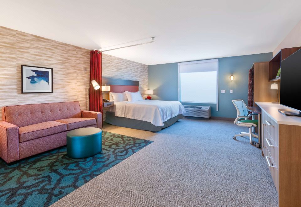 a modern hotel room with a bed , couch , and chair , as well as a tv , desk , and window at Home2 Suites by Hilton Battle Creek