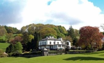 a large white building with a green lawn and trees in the background , under a cloudy sky at Ees Wyke Country House