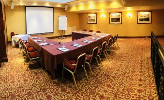 a conference room with multiple tables , chairs , and a projector screen , set up for meetings or presentations at Dryburgh Abbey Hotel