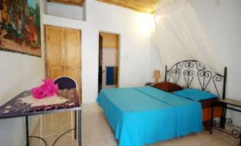 a bedroom with a bed , nightstand , and table , featuring a blue blanket and pink flower decoration at Hotel Maya