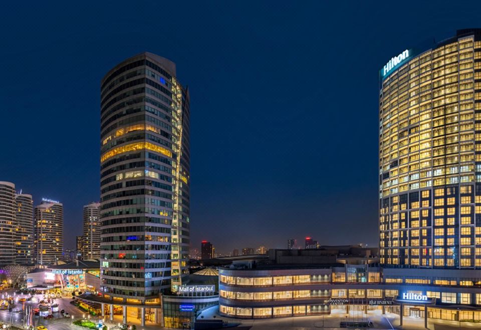 a city skyline at night , with two tall buildings illuminated and surrounded by a body of water at Hilton Mall of Istanbul