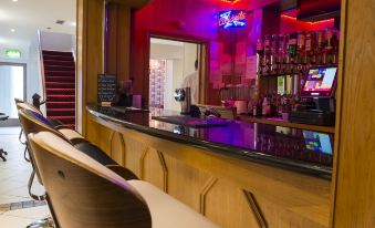 a bar with a purple and blue neon sign , two chairs , and a counter filled with liquor bottles at Kilmorey Arms Hotel