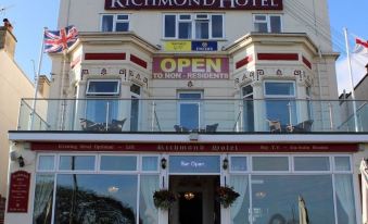 a large , two - story hotel building with multiple balconies and a red roof , situated on a sunny day at Richmond Hotel