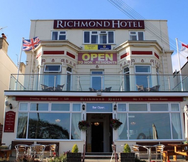 a large , two - story hotel building with multiple balconies and a red roof , situated on a sunny day at Richmond Hotel