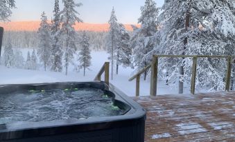 a hot tub is situated on a wooden deck overlooking snowy trees and mountains , with the sun setting in the background at Arctic Skylight Lodge