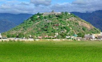 a mountainous landscape with a large building on top and green fields in the foreground at Jayam