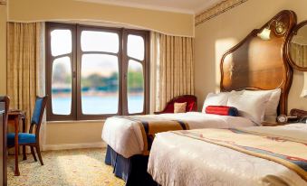 A bedroom with double beds, large windows, and a balcony that overlooks the waterfront at Shanghai Disneyland Hotel