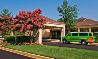 a green van is parked in front of a building with trees and bushes surrounding it at Courtyard New Carrollton Landover