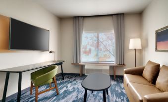 a small hotel room with a television , couch , and coffee table , along with a window with curtains at Fairfield Inn & Suites Houston League City