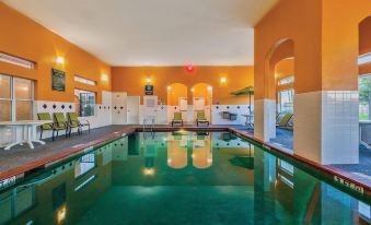 an indoor swimming pool with a large , empty space between the two lanes , surrounded by orange walls and a swimming area with lounge chairs at La Quinta Inn & Suites by Wyndham Houston Channelview