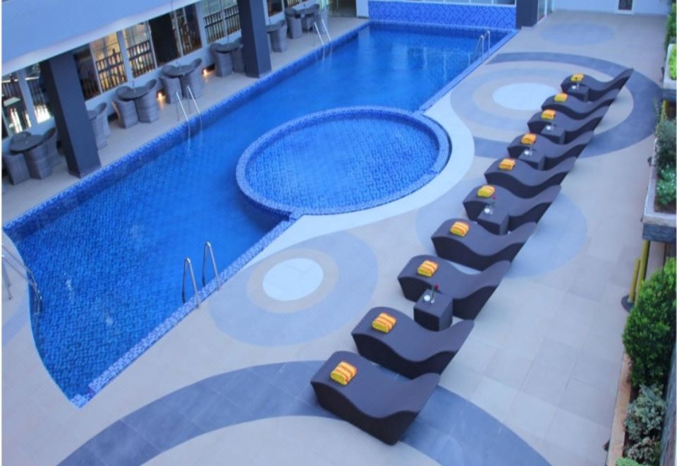 an indoor swimming pool surrounded by lounge chairs , with people enjoying their time in the pool area at Merapi Merbabu Hotels Bekasi