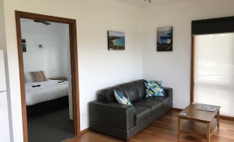 a living room with a brown leather couch , wooden coffee table , and two paintings on the wall at Prom Coast Holiday Lodge