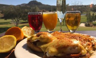 a plate of food , including a slice of pizza and two glasses of orange juice , is displayed on a table with a view of the mountains at San Vicente Golf Resort