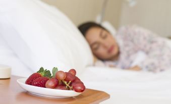 a person is lying in bed with a bowl of fruit on the side , and another person is sleeping in the background at Gatton Motel