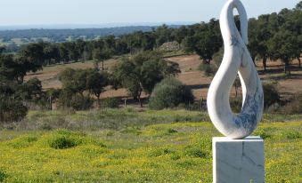 a white sculpture on a stone base in a grassy field , with trees and fields visible in the background at MirArte