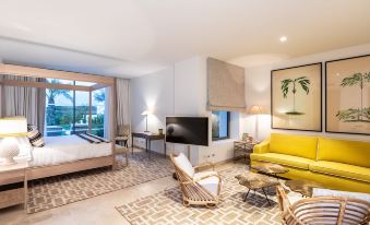 a modern living room with a yellow couch , wooden coffee table , and large windows that offer views of the outdoors at Finca Cortesin Hotel Golf & Spa