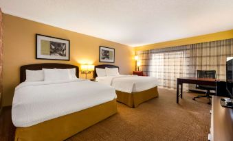 a hotel room with two beds , a window , and framed pictures on the wall , along with wooden furniture and a desk at Sonesta Select Detroit Novi