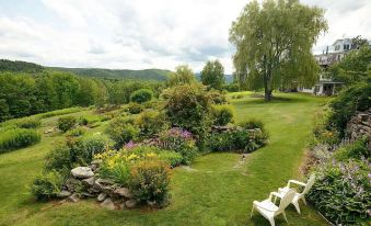 a lush green garden with a variety of flowers and plants , surrounded by trees and hills at Windham Hill Inn
