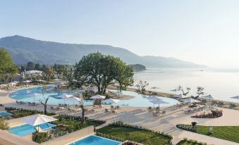 a large resort with multiple swimming pools , umbrellas , and sun loungers , surrounded by lush greenery and mountains at Ikos Dassia