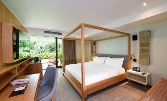 a large bed with a wooden frame and white sheets is in a room with a chair , desk , and sliding glass door at Tabacón Thermal Resort & Spa