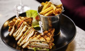 a sandwich and french fries are served on a plate next to a glass of wine at Mercure York Fairfield Manor Hotel
