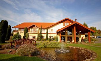 a large house with a red roof and a fountain in front of it , surrounded by greenery at Tamar Valley Resort Grindelwald