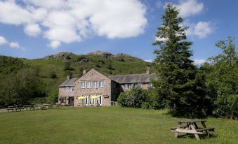 a large house is situated on a hillside with a picnic area in front of it at YHA Eskdale