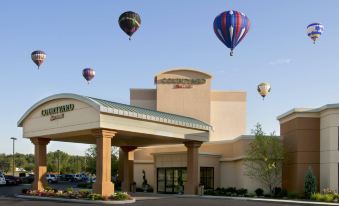 a hotel with a covered entrance and several hot air balloons floating in the sky above at Courtyard Canton