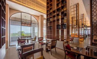 a modern restaurant with wooden furniture , large windows offering views of the city and mountains , and comfortable seating arrangements at Hilton Goa Resort