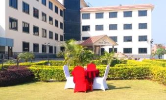 a large building with a red sign is in the background of a lawn with chairs and a white table at Suva Hotel
