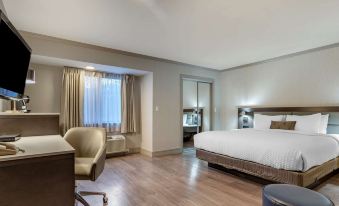 a hotel room with a king - sized bed , a desk , a chair , and a bathroom in the background at Best Western Plus Executive Suites