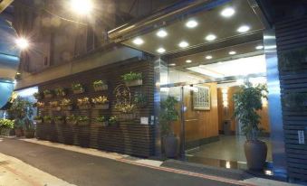 a building entrance with a row of potted plants on the wall and an entrance door at Han She Business Hotel