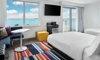 a hotel room with a large window overlooking the ocean , featuring a bed , television , and colorful rug at Aloft Ocean City